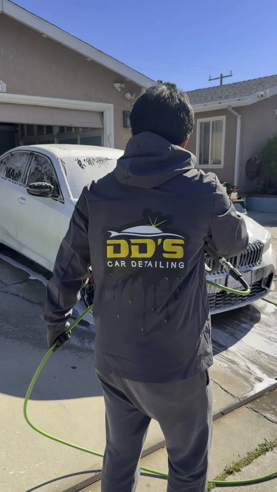 DD's detailer pressure-rinsing a foamed BMW at a client's home